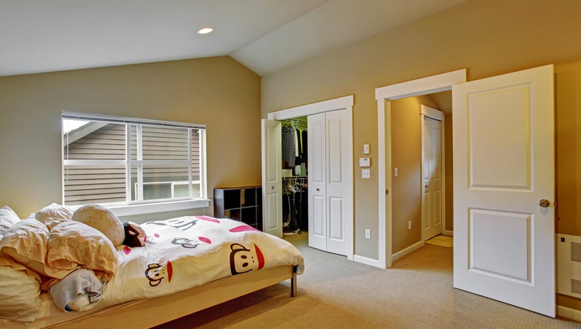 Cozy bedroom with high vaulted ceiling and walk in closet. Light wooden bed with white cheerful bedding